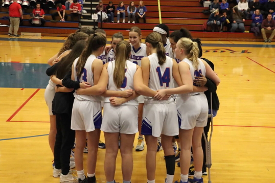 The girls varsity basketball team huddling at one of their games.